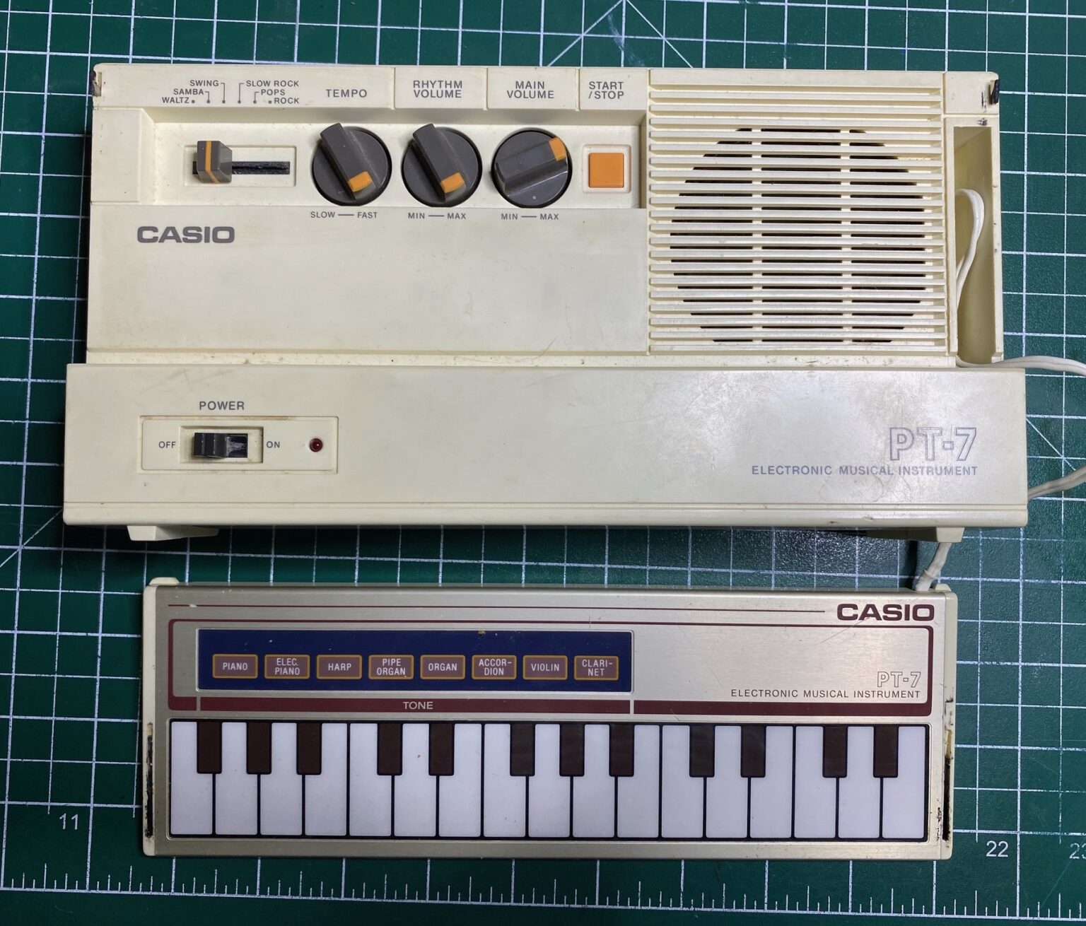 A Casio PT-7, with its keyboard on display. The keyboard is a thin film touch keyboard, and the main body is beige with a rhythm selector slider, three knobs for tempo and tone, and a start/stop button for accompaniment. A speaker grille fills the right third of the small unit.