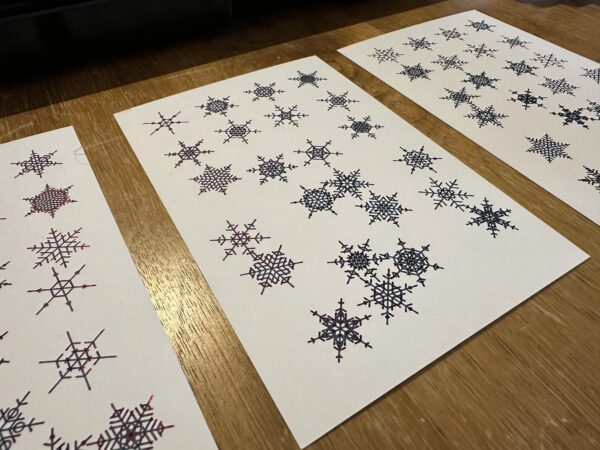 Three white postcards, with randomly generated snowflakes drawn on them in a green ink with a red sheen.