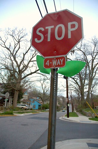 A stop sign that has two large leaves added to the post, just below the sign, making it look like a large rose