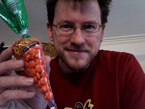 A picture of me holding a very narrow plastic bag full of orange Reese's Pieces, which makes it look as if it were a stylized carrot