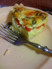 A piece of quiche sits on a pale yellow plate, with a metal fork